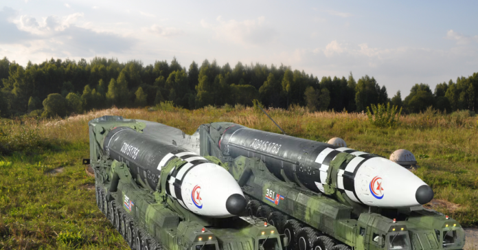 Two North Korean ballistic missiles mounted on mobile launchers, stationed in a grassy field under a clear sky.